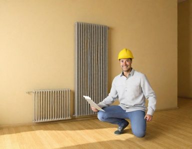 Un homme en casque de chantier inspecte une pièce vide avec un radiateur.