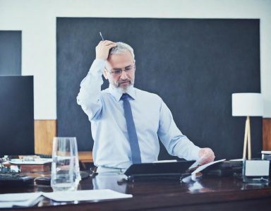 Homme d'affaires en chemise, pensif, devant un bureau avec un téléphone et un verre d'eau.